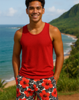 Man wearing a red tank top and floral tropical shorts standing in a scenic location with ocean and mountains.