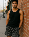 Man with black tank top and RF-Wear Men's Mesh Bandana Shorts in Black leaning against a brick wall.