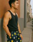 Man wearing a black tank top and star-patterned shorts standing against a wall.