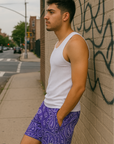 Man leaning against wall on city sidewalk wearing RF-Wear Men's Mesh Bandana Shorts in Purple.
