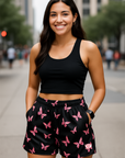 Woman wearing a black crop top and black shorts with pink butterfly pattern on a city street.