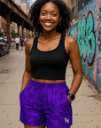 Woman wearing a black tank top and purple shorts/black butterflies with a city street and graffiti in the background