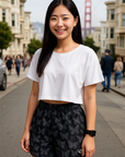 Woman in a white crop top and black butterfly patterned shorts standing on a city street.