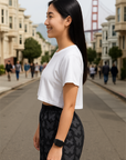Woman in a white crop top and black butterfly patterned shorts standing on a city street.