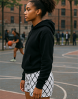 Person wearing a black hoodie and white shorts with black chain link pattern on a basketball court.