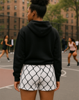 Person wearing a black hoodie and white shorts with black chain link pattern on a basketball court.