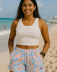 Woman in a white tank top and blue shorts with pink leaf pattern on a beach.
