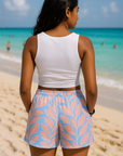 Person wearing a white top and pink leaf-patterned shorts on a beach.
