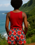 Person wearing a red tank top and floral shorts standing with their back to the camera, overlooking a scenic ocean view with mountains.