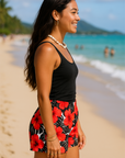Woman wearing a black tank top and coral on black white floral tropical shorts on a beach.