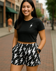 Woman wearing a black crop top and black and white lightning bolt patterned shorts on a city street.