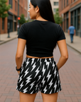 Woman wearing a black crop top and black and white lightning bolt patterned shorts on a city street.