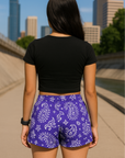 Woman standing on city sidewalk wearing RF-Wear Women's Paisley Shorts - Purple/White - Back View