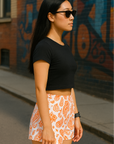 Woman wearing a black crop top and RF-Wear white/orange paisley shorts standing in front of a graffiti-covered wall.