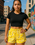 Woman standing on city sidewalk wearing RF-Wear Women's Paisley Shorts - Yellow/White - Front View