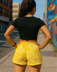 Woman standing on city sidewalk wearing RF-Wear Women's Paisley Shorts - Yellow/White - Back View