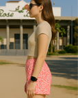 Woman wearing sunglasses and a beige top with RF-Wear women's rose shorts in pink/white in front of a building.