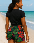 Woman in black cropped top and colorful shorts standing on the beach.