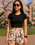 Person wearing a black crop top and RF-Wear blossom shorts in cream/pink on a college campus with cherry blossom trees.