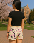 Person wearing a black crop top and RF-Wear blossom shorts in cream/pink on a college campus with cherry blossom trees.