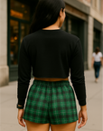 Person wearing a black long-sleeve top and green plaid shorts on a city street.