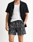 Man wearing a white tank top with unbuttoned black short sleeve shirt and RF-Wear Men's Aztec Print Shorts