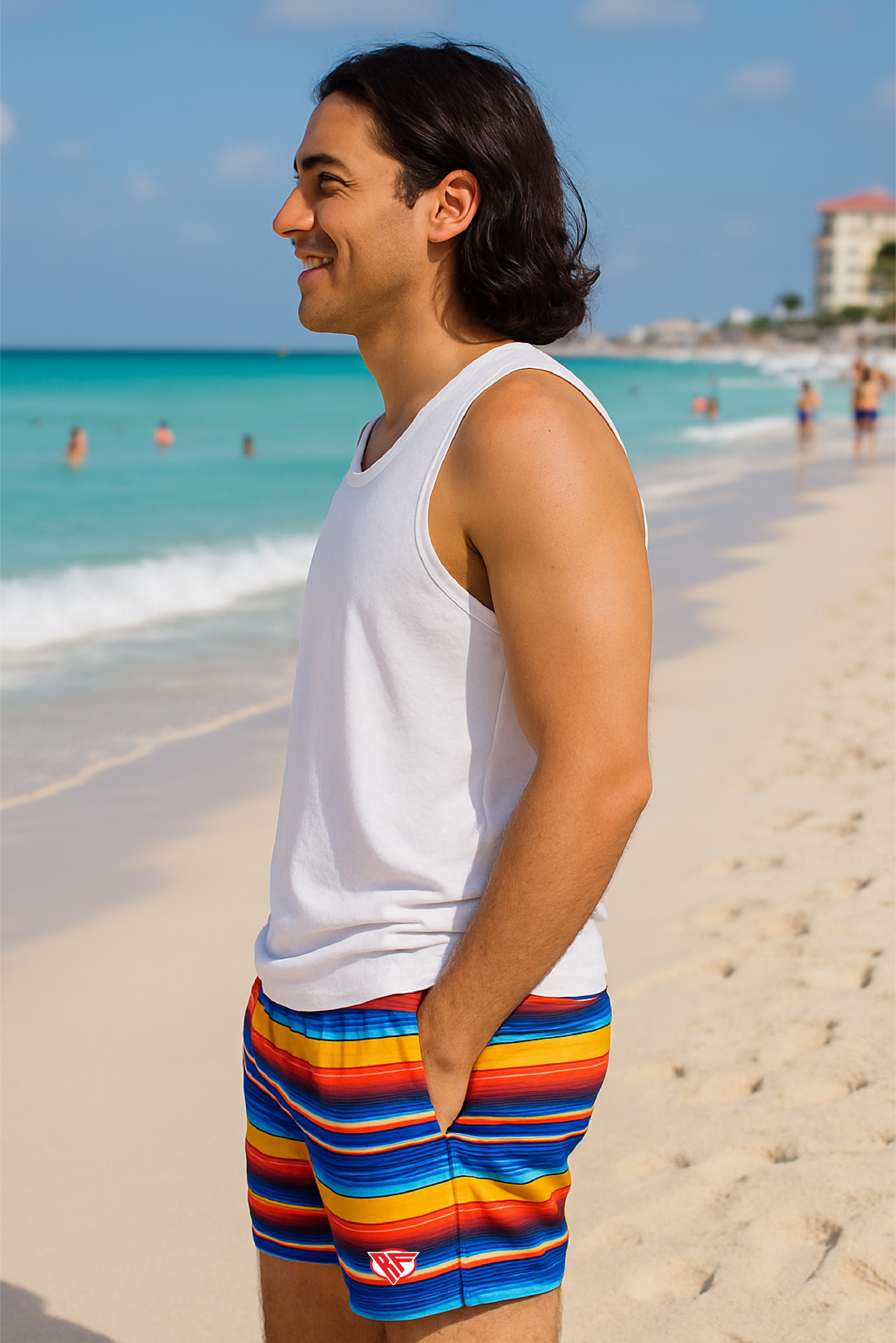 Man in blue top and colorful striped shorts standing on a beach with ocean and sky in the background