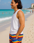 Man in blue top and colorful striped shorts standing on a beach with ocean and sky in the background