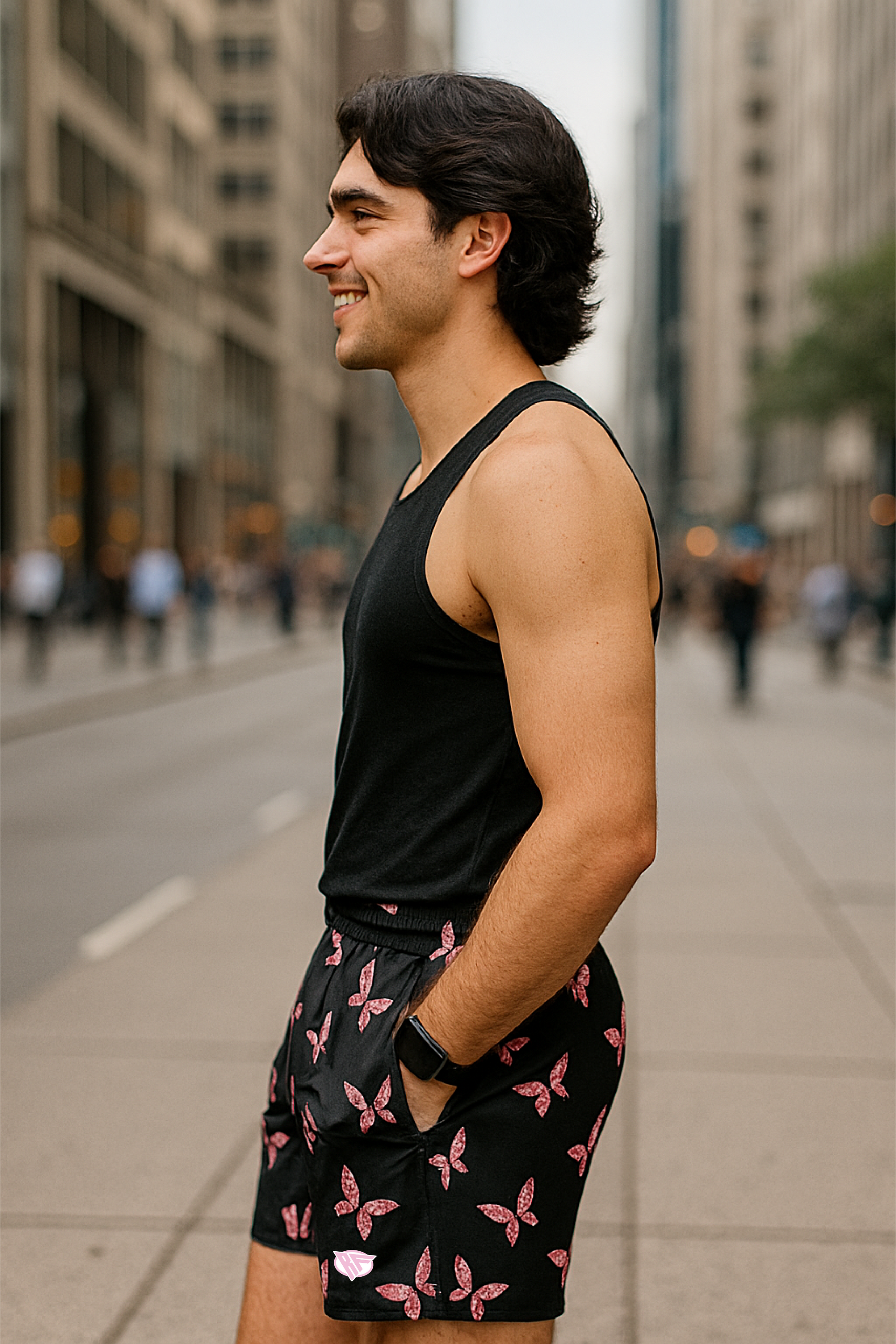 Man in black tank top and butterfly patterned shorts standing on a city street