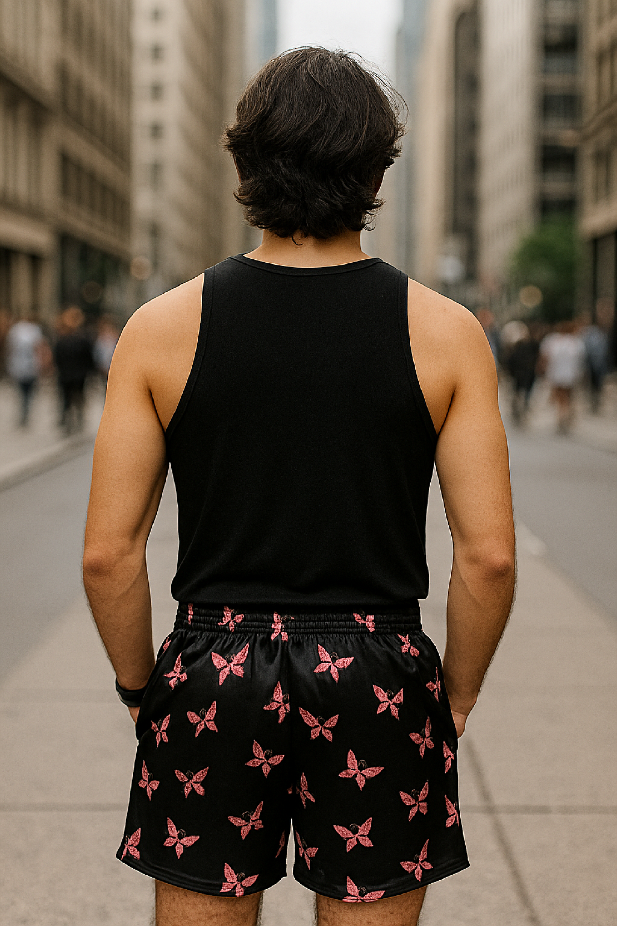 Person wearing a black tank top and black shorts with pink butterfly patterns on a city street.