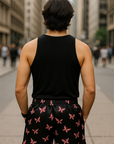 Person wearing a black tank top and black shorts with pink butterfly patterns on a city street.