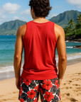 Man wearing a red tank top and floral tropical shorts on a beach with mountains in the background