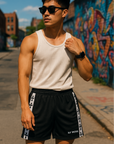 Man standing on street with graffiti in background wearing a white tank top and RF-Wear side trim cross shorts in black/white.