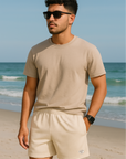 Man standing on beach wearing a cream t-shirt and RF-Wear Men's Mesh Solid Color Shorts in Cream. 