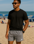Man on beach wearing a solid color black t-shirt and RF-Wear Men's Mesh Solid Color  Shorts in Grey 