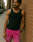 Man on standing on sidewalk leaning against a brick wall wearing a black tank top and RF-Wear Men's Mesh Bandana Shorts in Fuchsia.