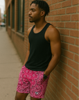 Man on standing on sidewalk leaning against a brick wall wearing a black tank top and RF-Wear Men's Mesh Bandana Shorts in Fuchsia.