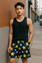 Man wearing a black tank top and navy shorts with star patterns on a city street.