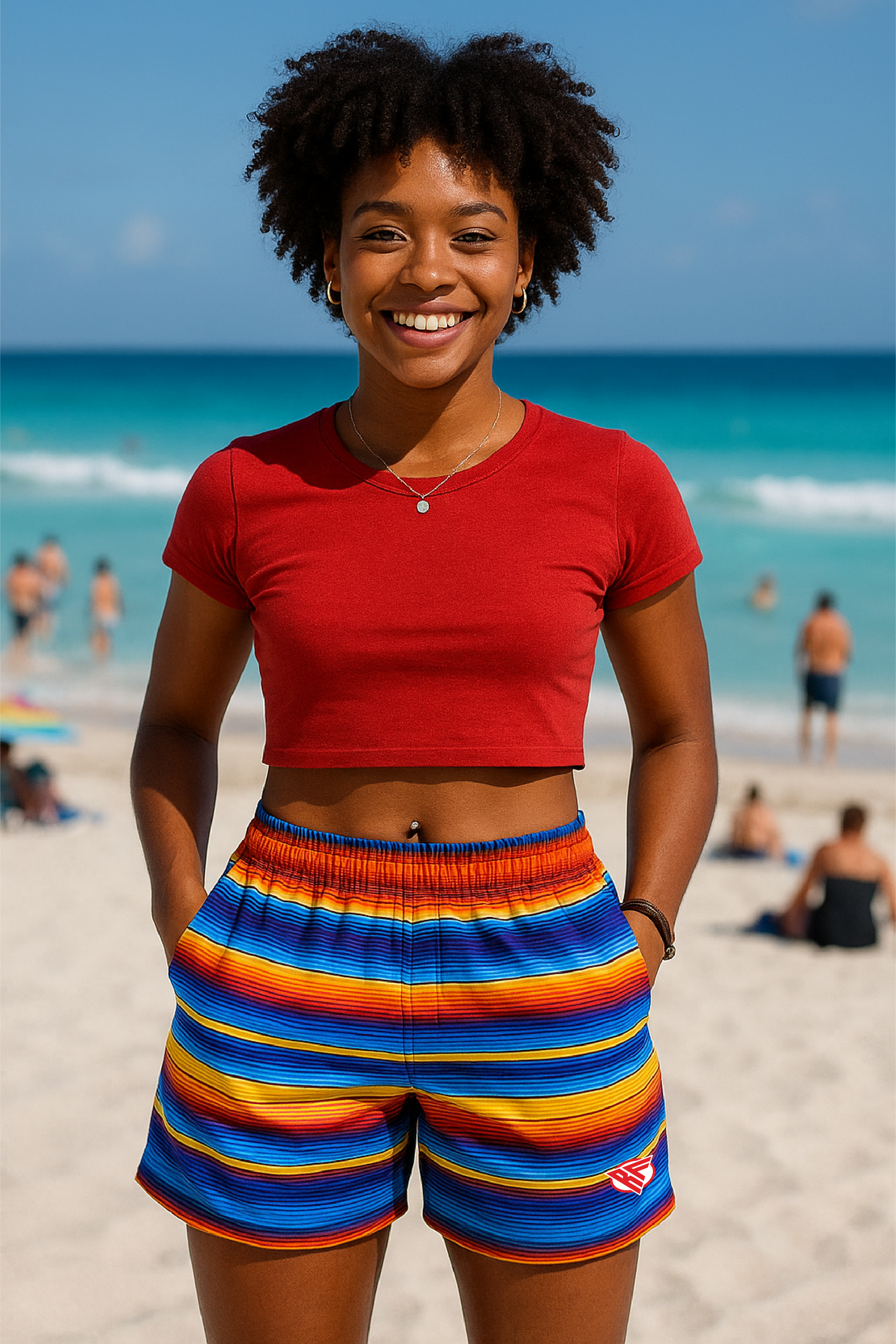 Woman in red top and colorful shorts standing on a beach with ocean in the background