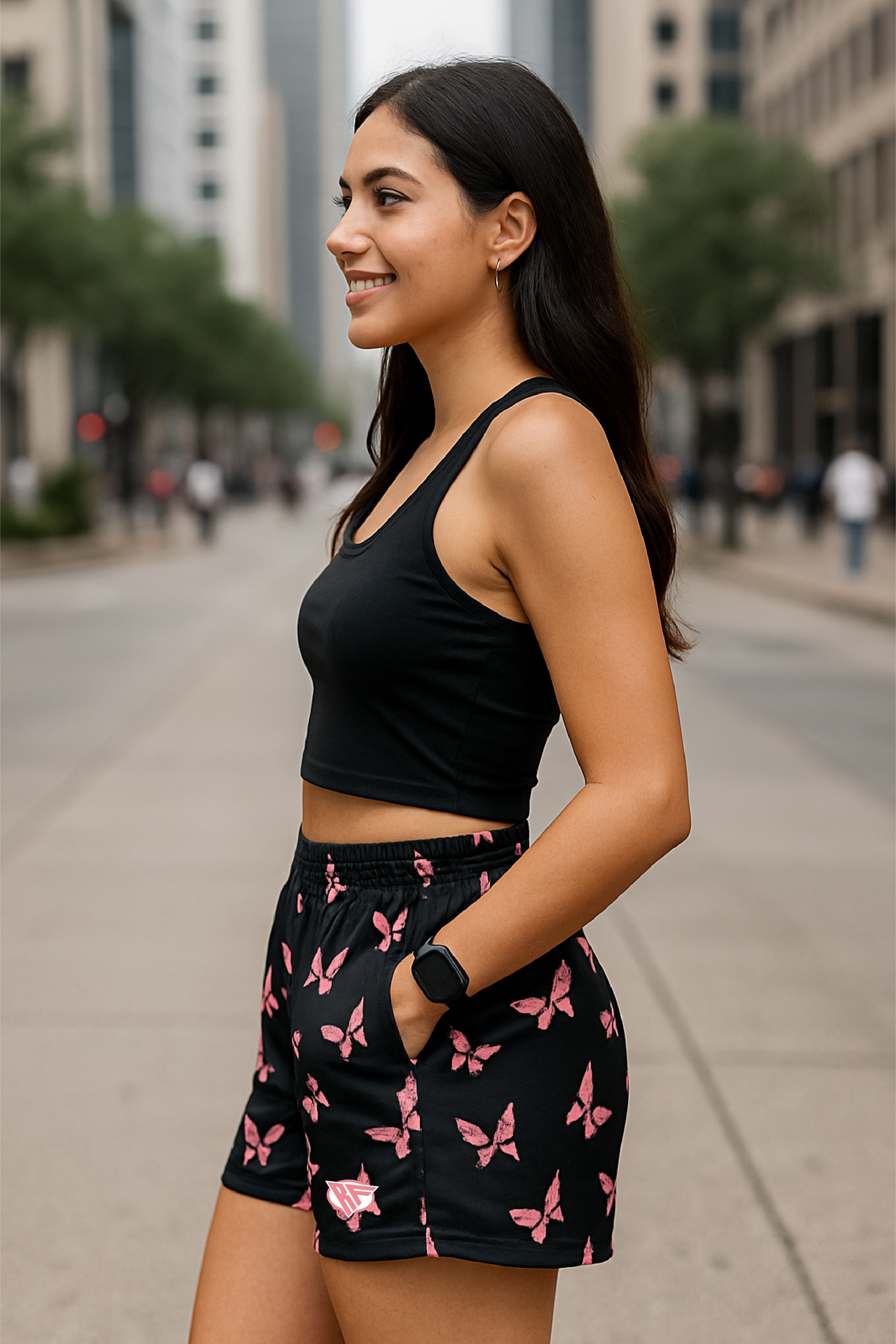 Woman wearing a black crop top and black shorts with pink butterfly pattern on a city street.