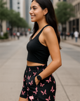 Woman wearing a black crop top and black shorts with pink butterfly pattern on a city street.