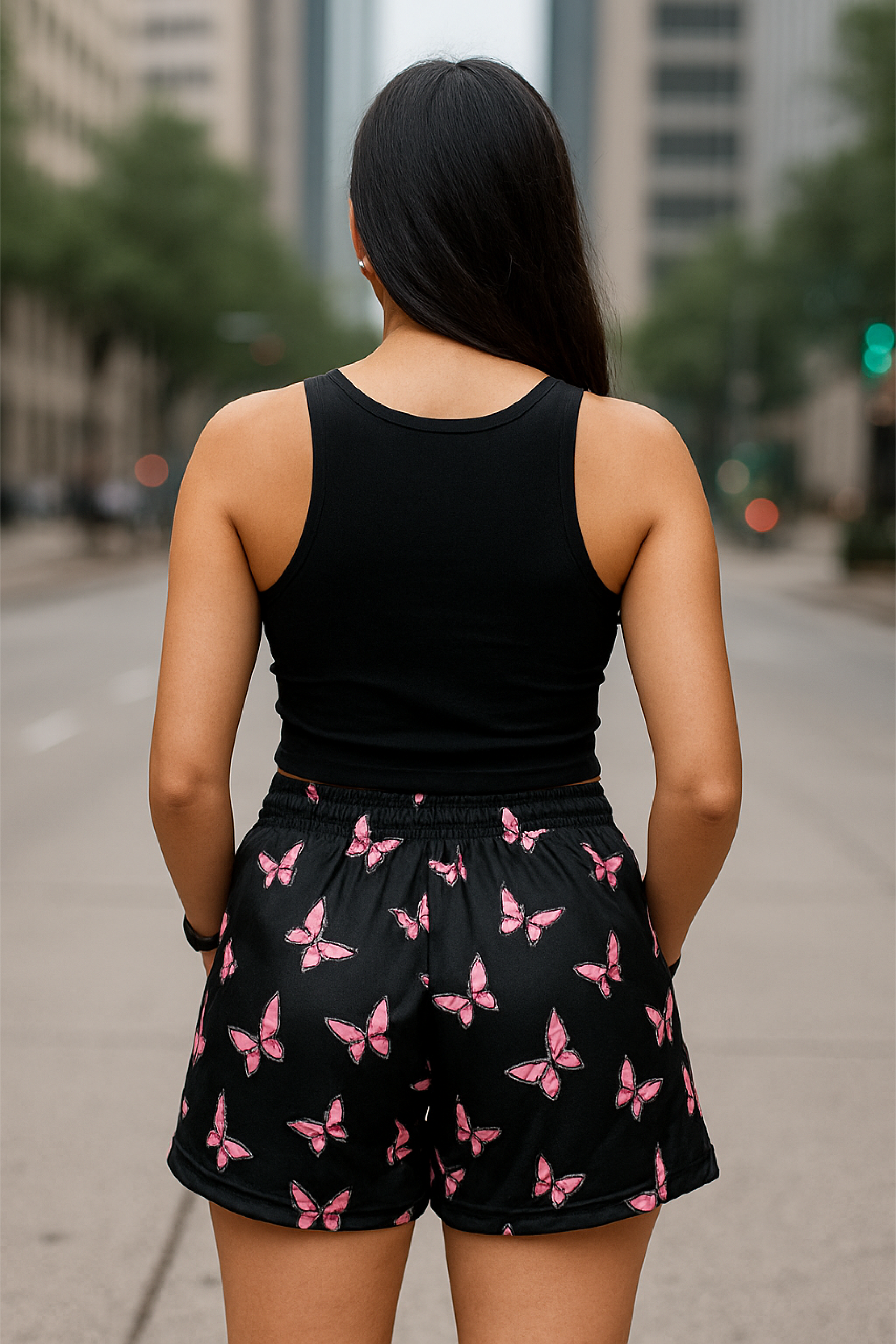 Woman wearing a black tank top and black shorts with pink butterfly pattern on a city street.