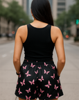 Woman wearing a black tank top and black shorts with pink butterfly pattern on a city street.