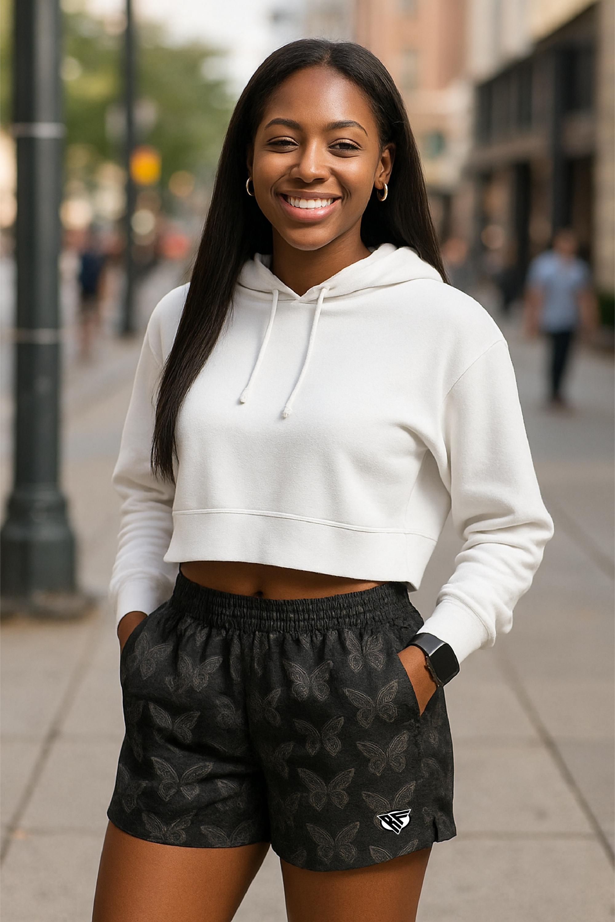 Woman wearing a white hoodie and black with white butterfly patterned shorts on a city street.
