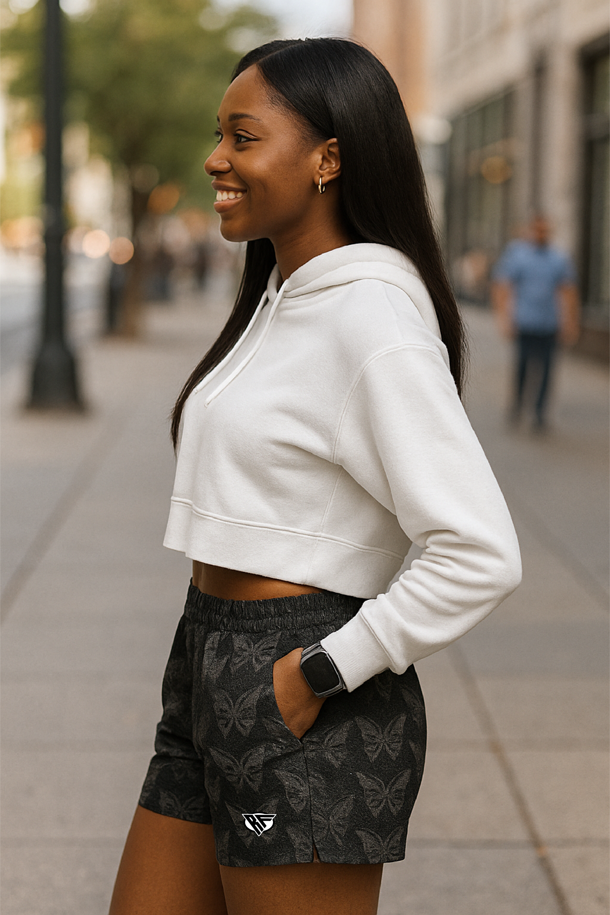 Woman wearing a white hoodie and black with white butterfly patterned shorts on a city street.