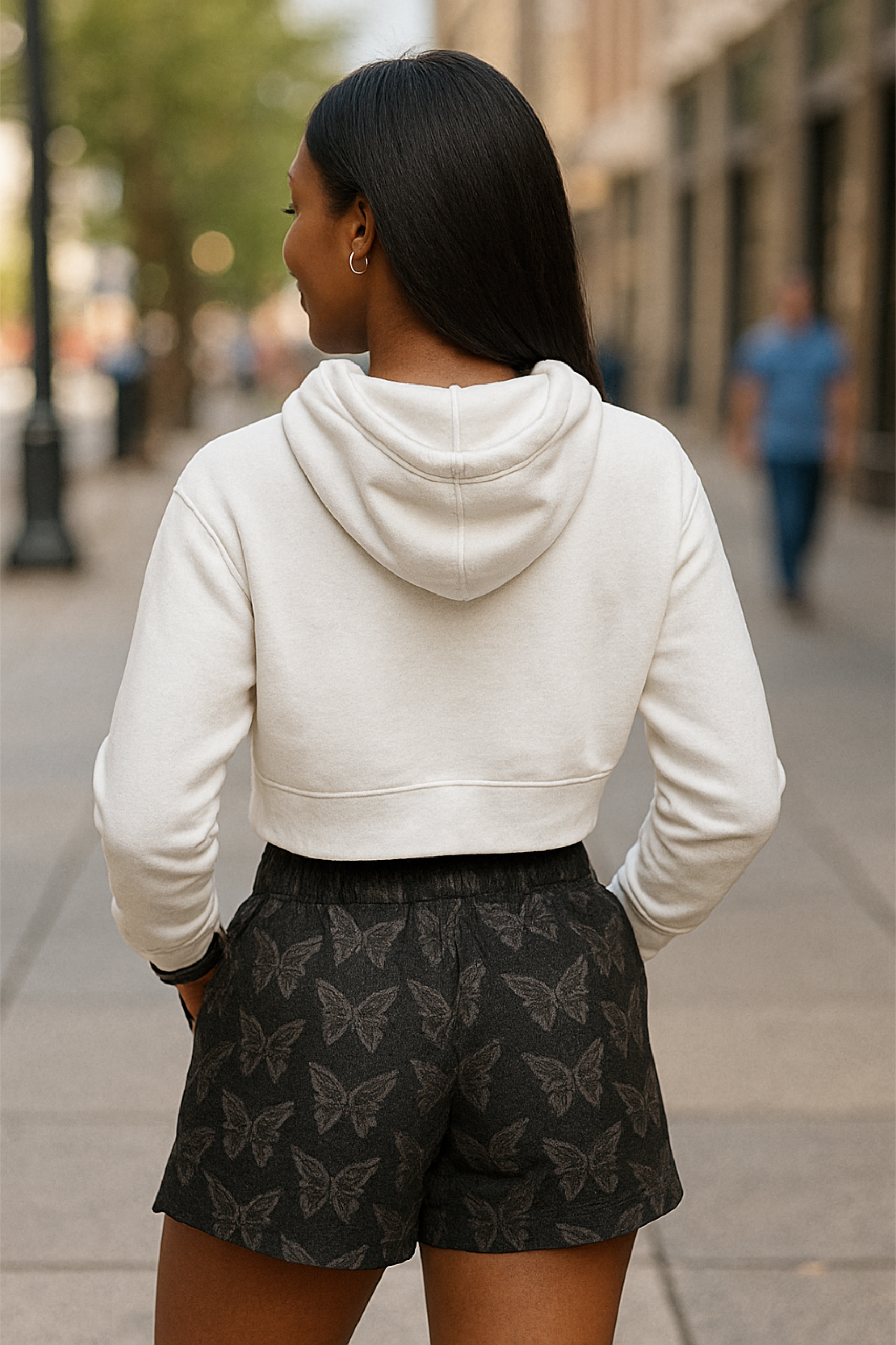 Woman wearing a white hoodie and black with white butterfly patterned shorts on a city street.