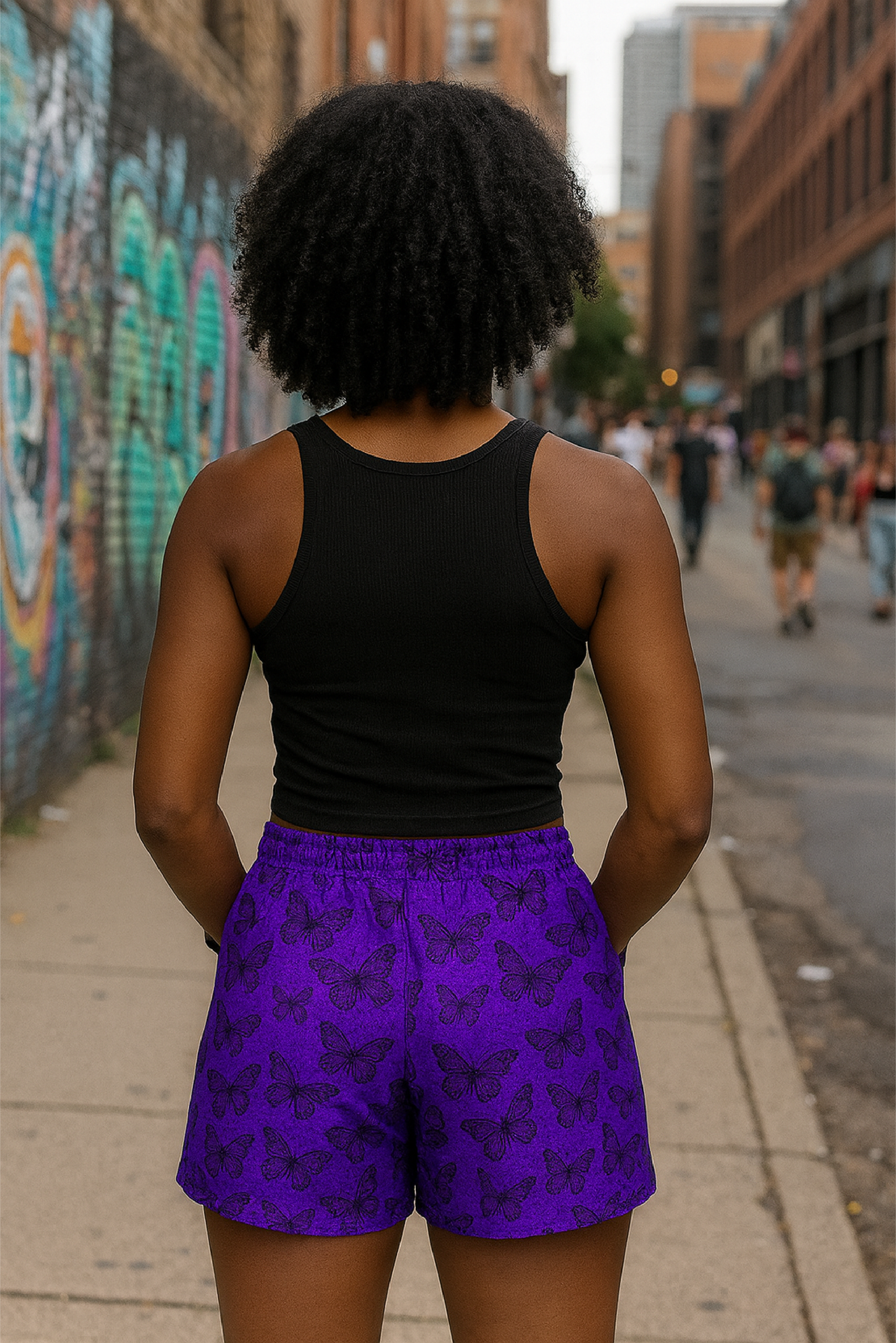 Women wearing a black tank top and purple shorts with black butterflies standing on a city street with graffiti.