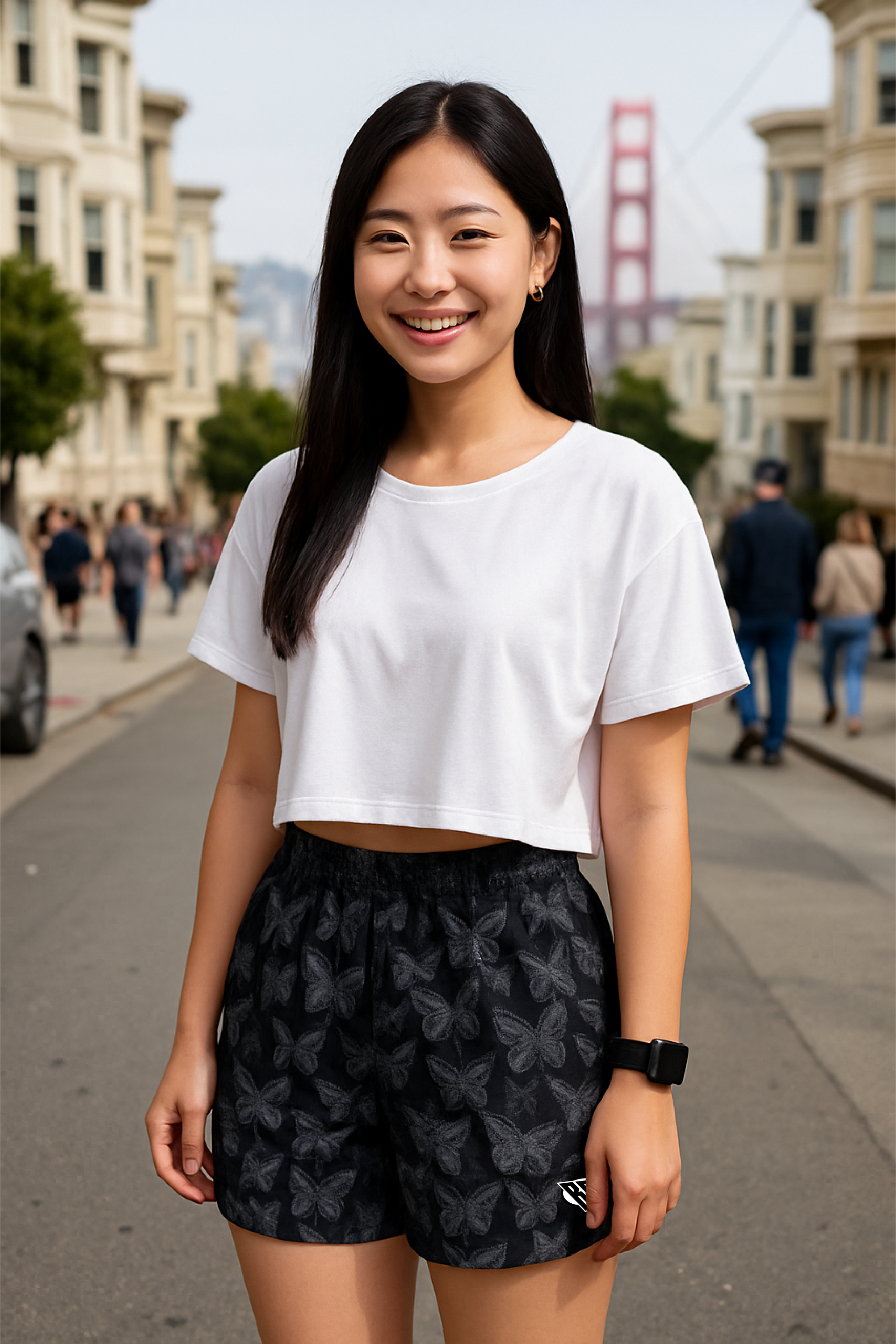Woman in a white crop top and black  butterfly patterned shorts standing on a city street.