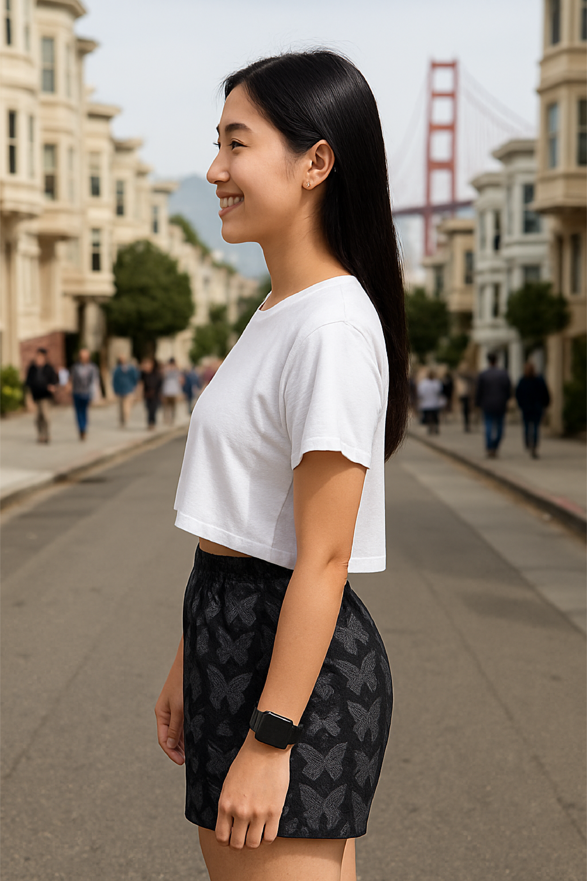 Woman in a white crop top and black  butterfly patterned shorts standing on a city street.