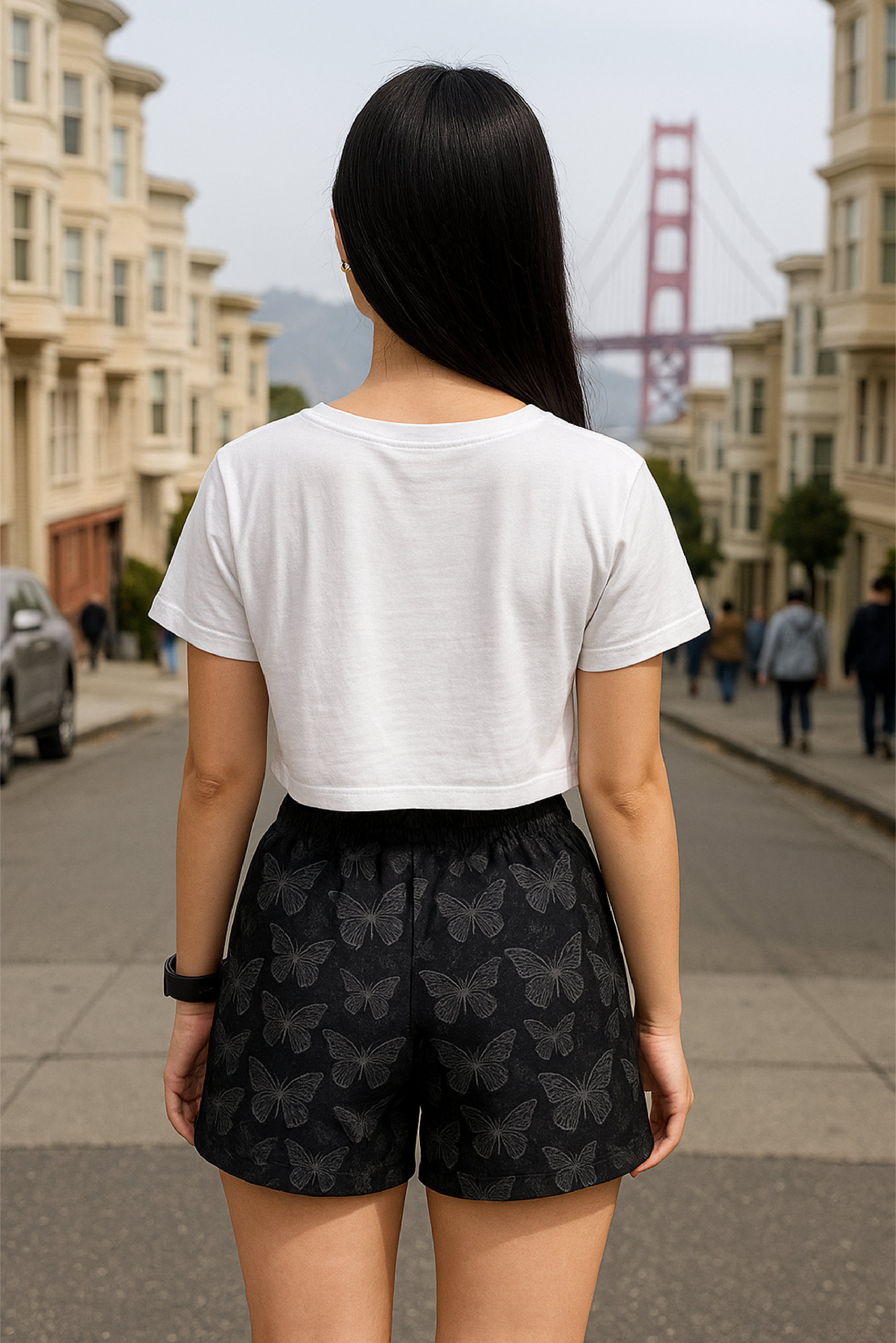 Woman in a white crop top and black  butterfly patterned shorts standing on a city street.